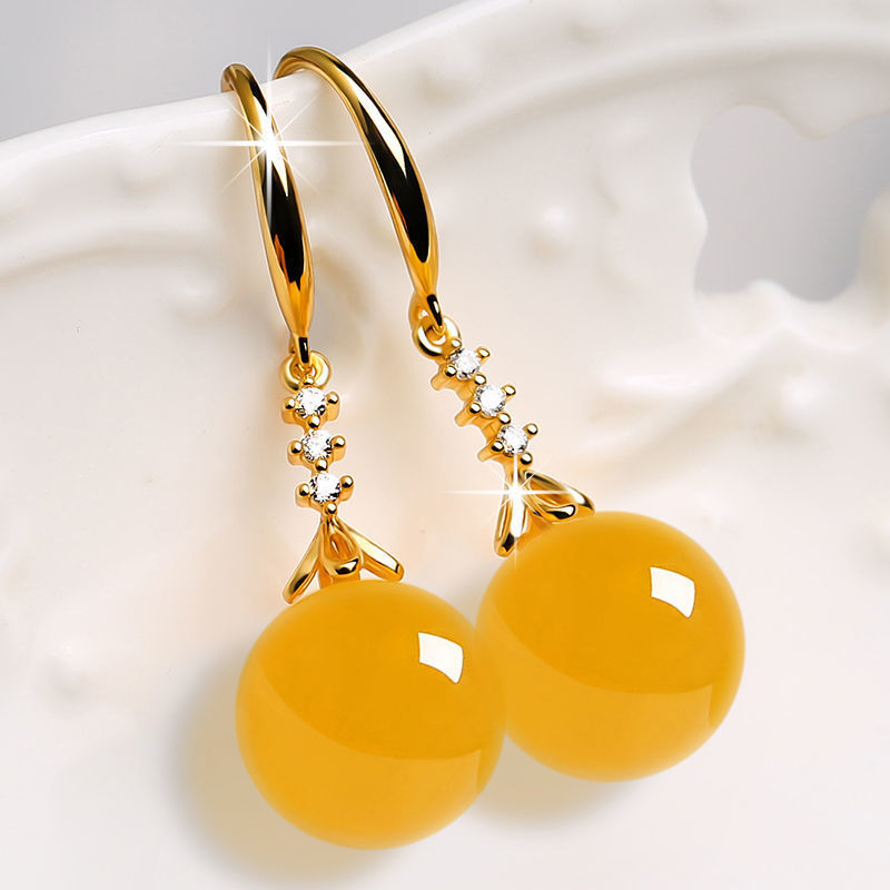 Gold earrings with yellow spherical stones on a white background