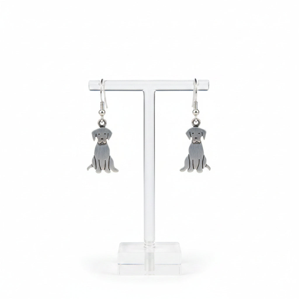 Silver dog-shaped earrings hanging on a rod with a hand holding one of them.