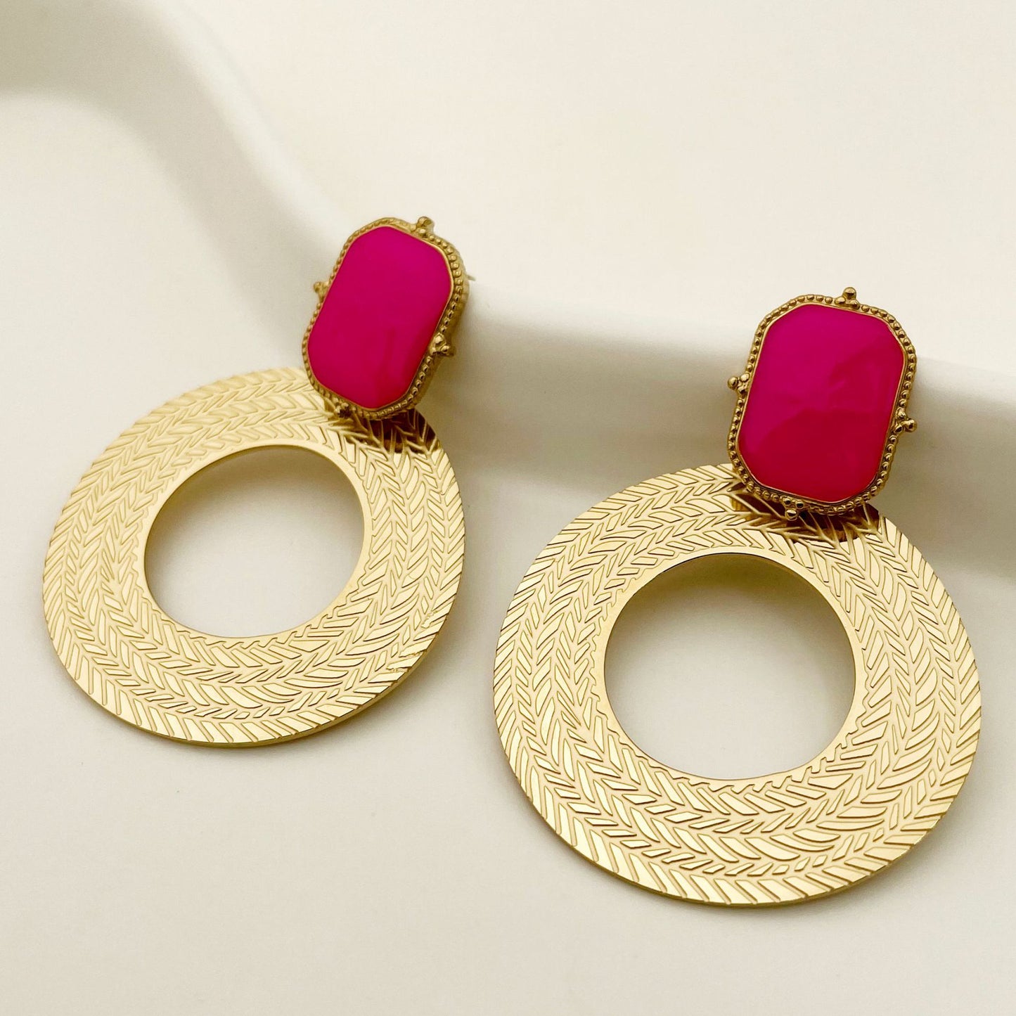 Gold earrings with pink stones on a beige background