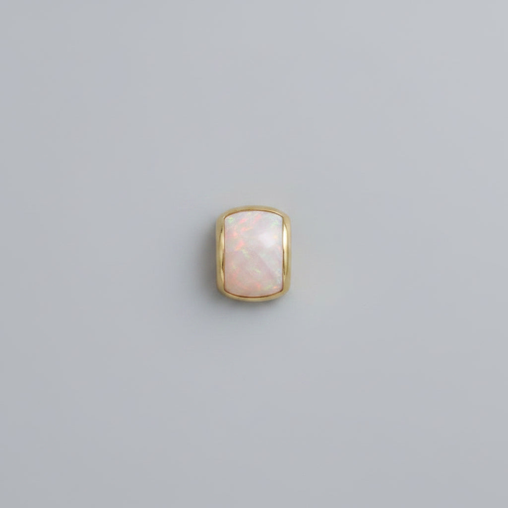 Close-up of a person wearing a gold earring with a stone in a neutral setting