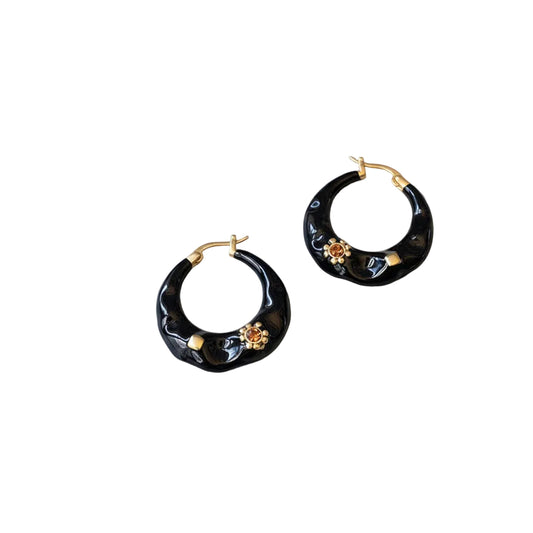 Black hoop earrings with gold accents on a gray surface