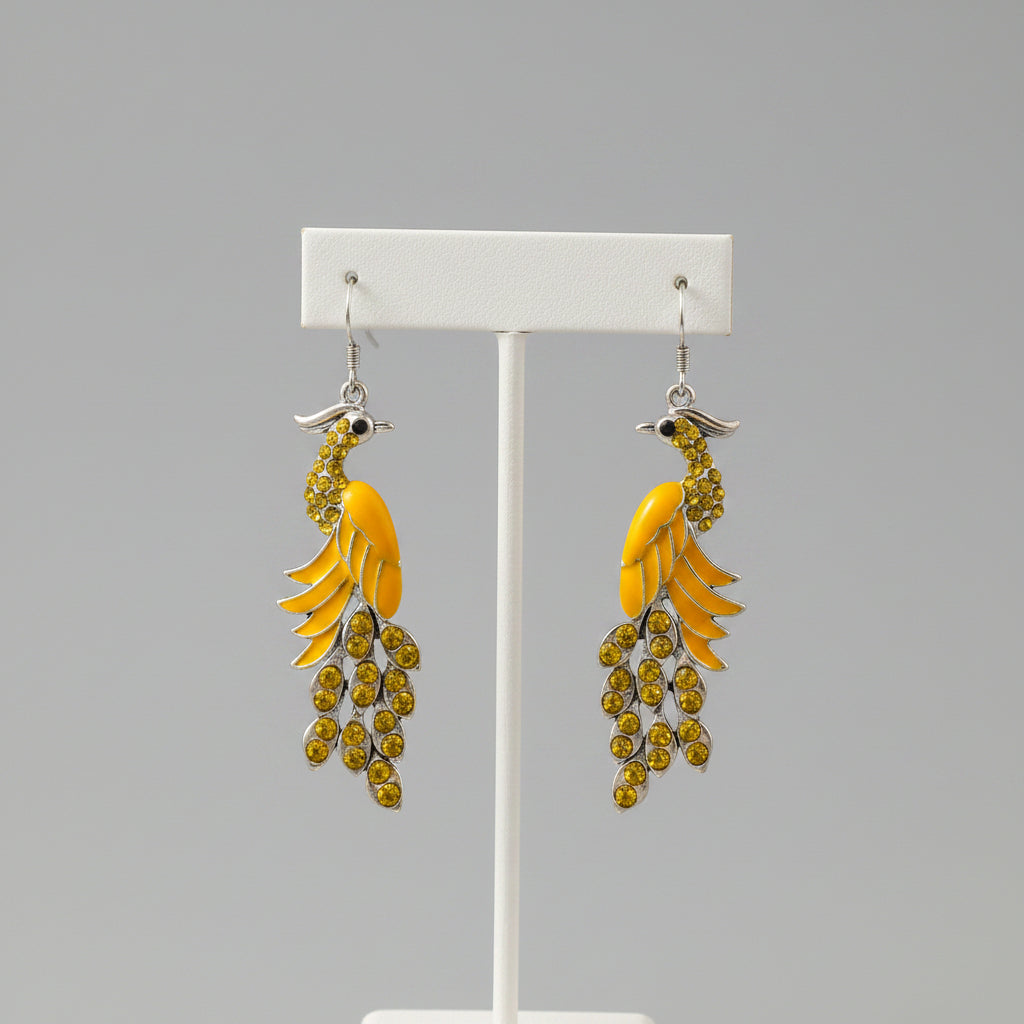 Pair of peacock feather earrings with yellow and green stones on a beige surface.