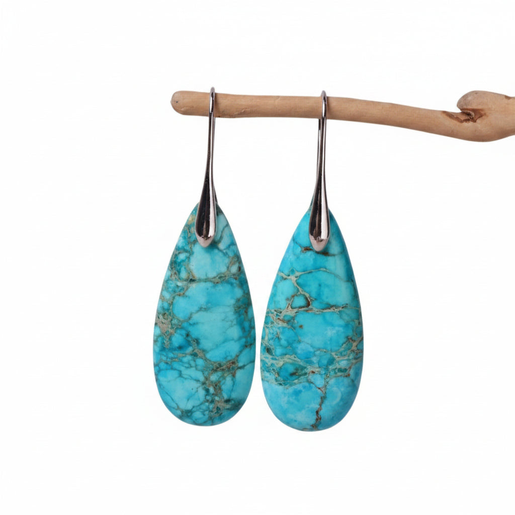 Turquoise teardrop earrings on a wooden stand against a light gray background