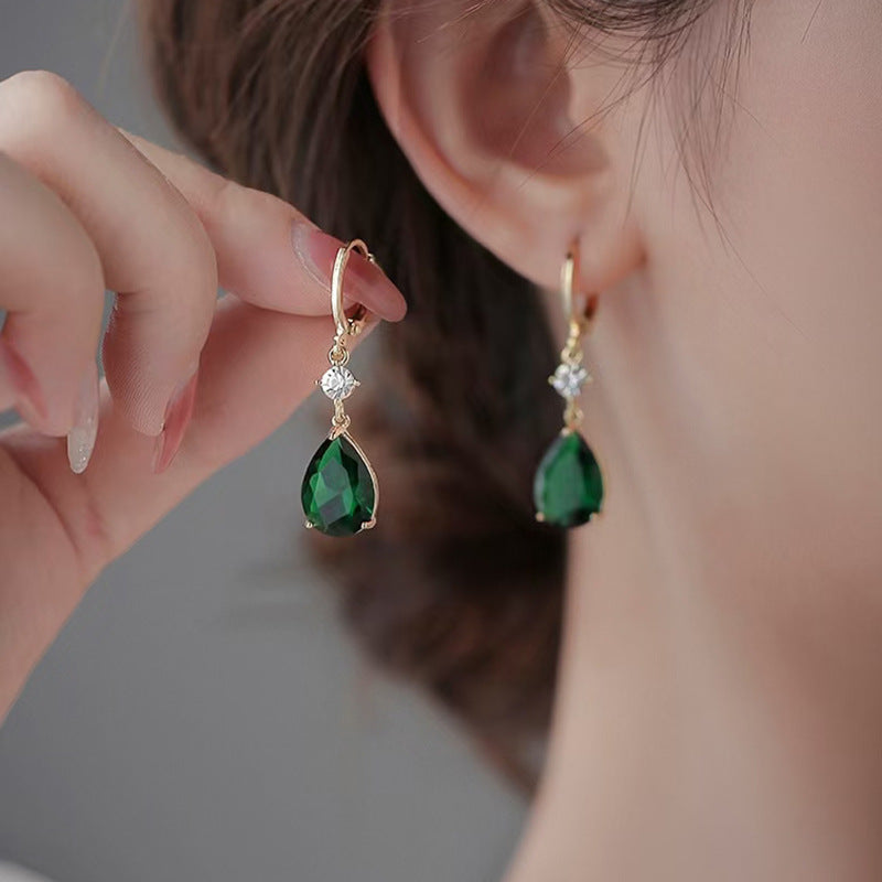 Close-up of a person wearing gold earrings with green gemstones.