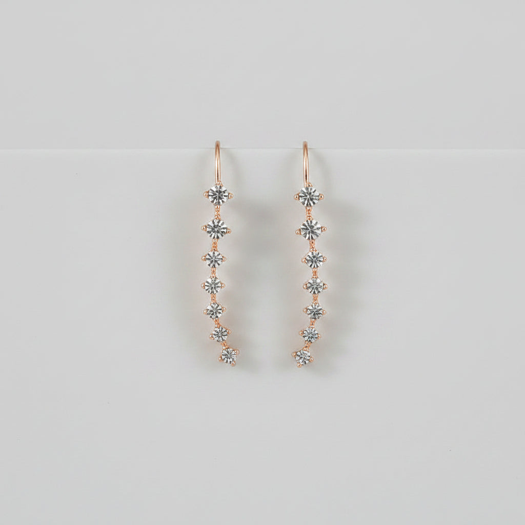 Rose gold earrings with clear stones on a white surface with flowers in the background