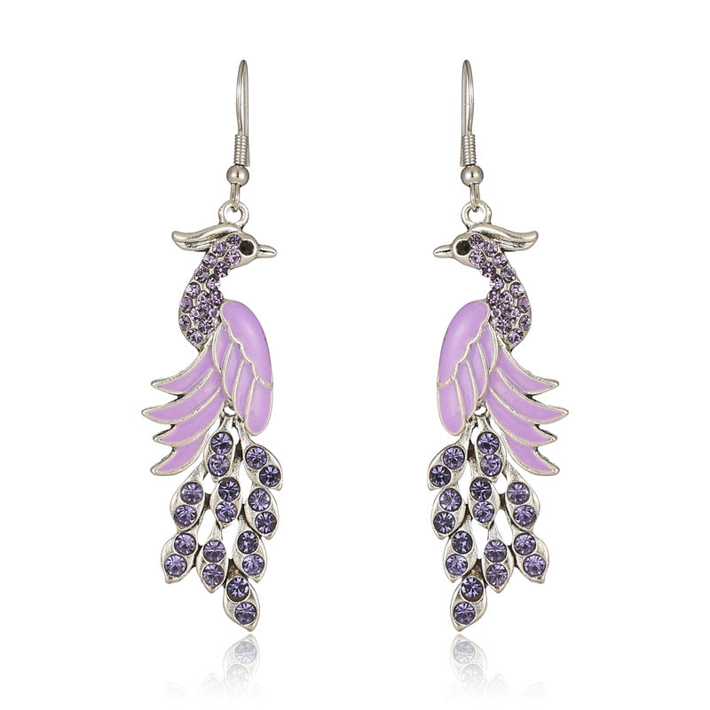 Purple peacock feather earrings with silver hooks on a white background