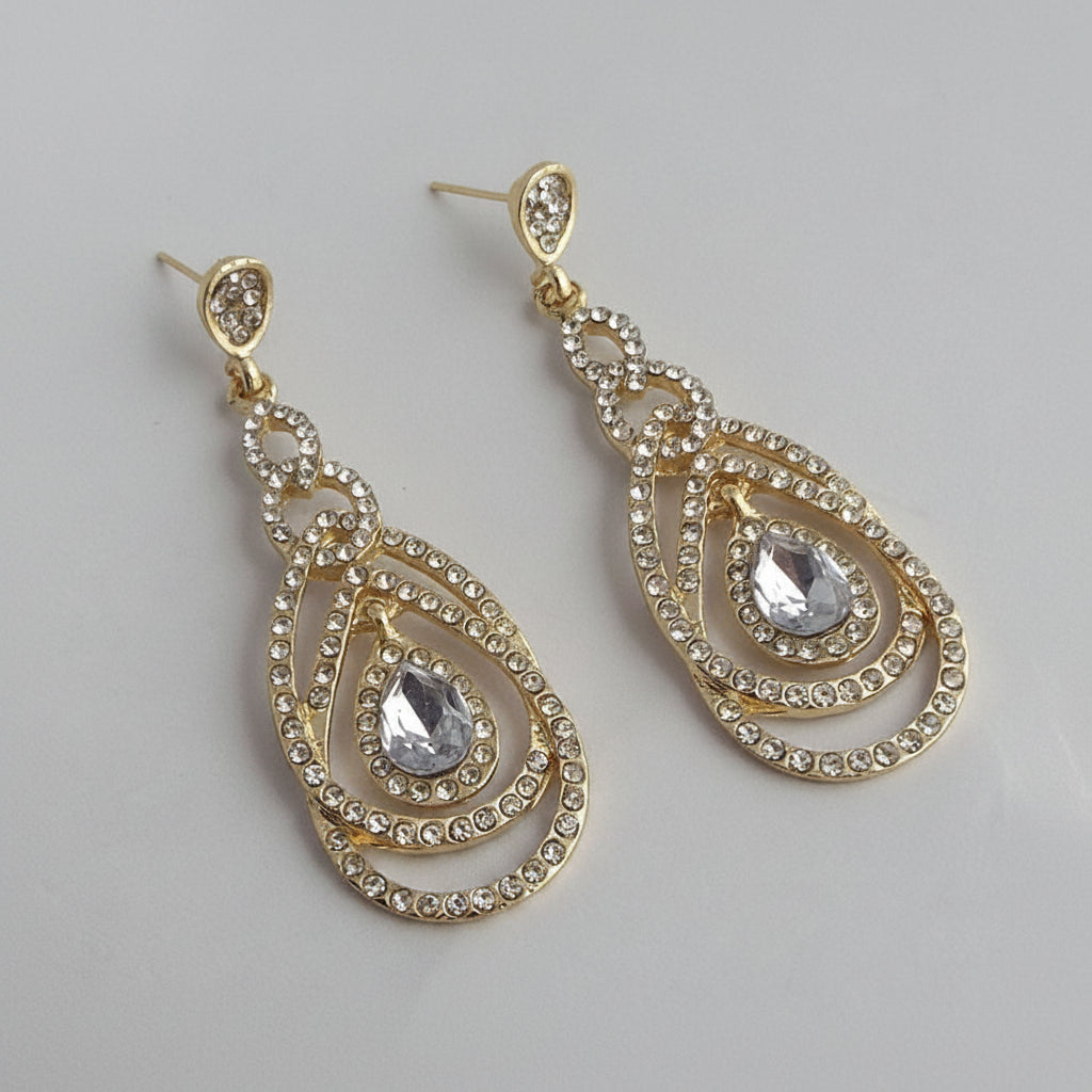 Gold and crystal teardrop earrings on a light gray background