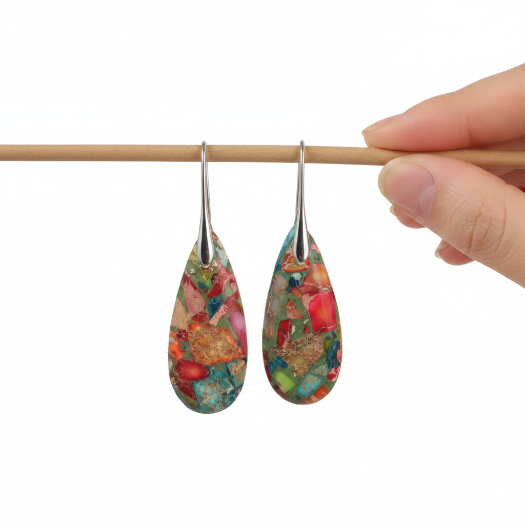 Colorful teardrop-shaped earrings on a wooden stick against a beige background