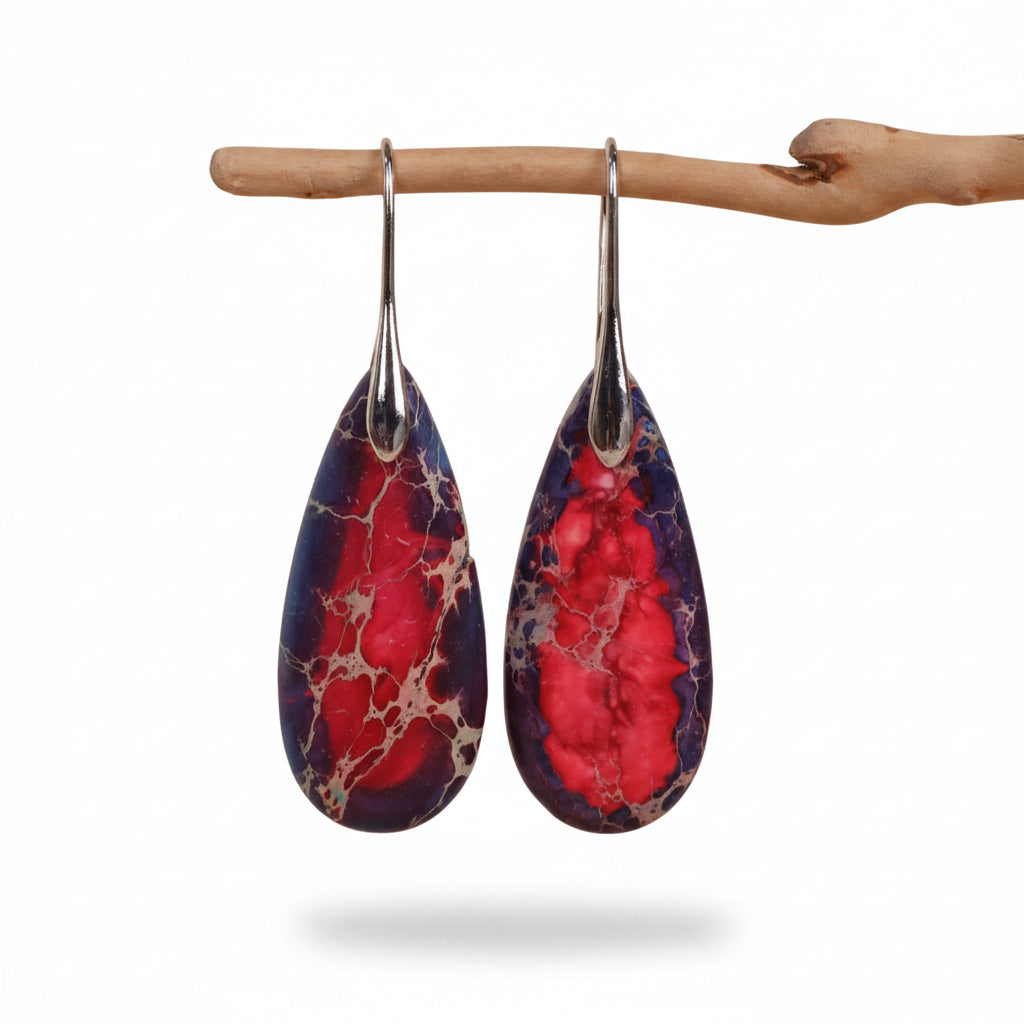 Teardrop-shaped earrings with red and purple marbled design hanging on a branch against a beige background