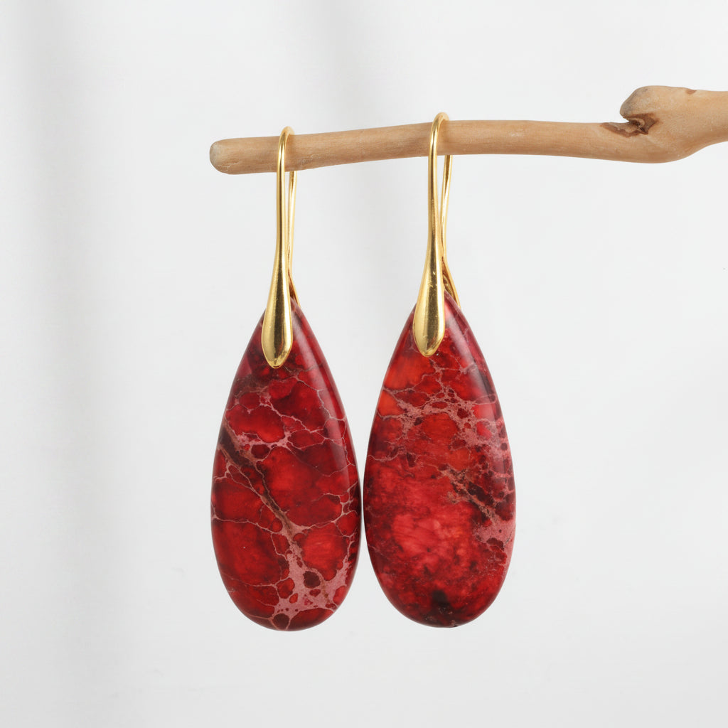 Red marbled teardrop earrings with gold hooks on a beige background
