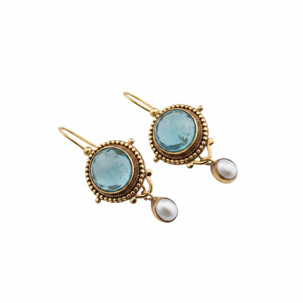 Ornate earrings with gold frames and blue gemstones on a gray surface.