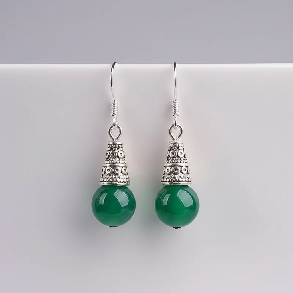 Green earrings with silver tops on a white cup