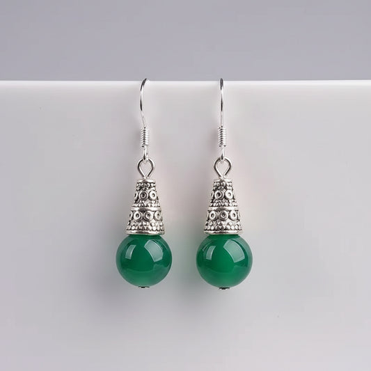 Green earrings with silver tops on a white cup