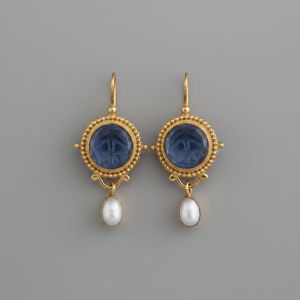 Gold earrings with blue gemstones and pearl drops on a gray background