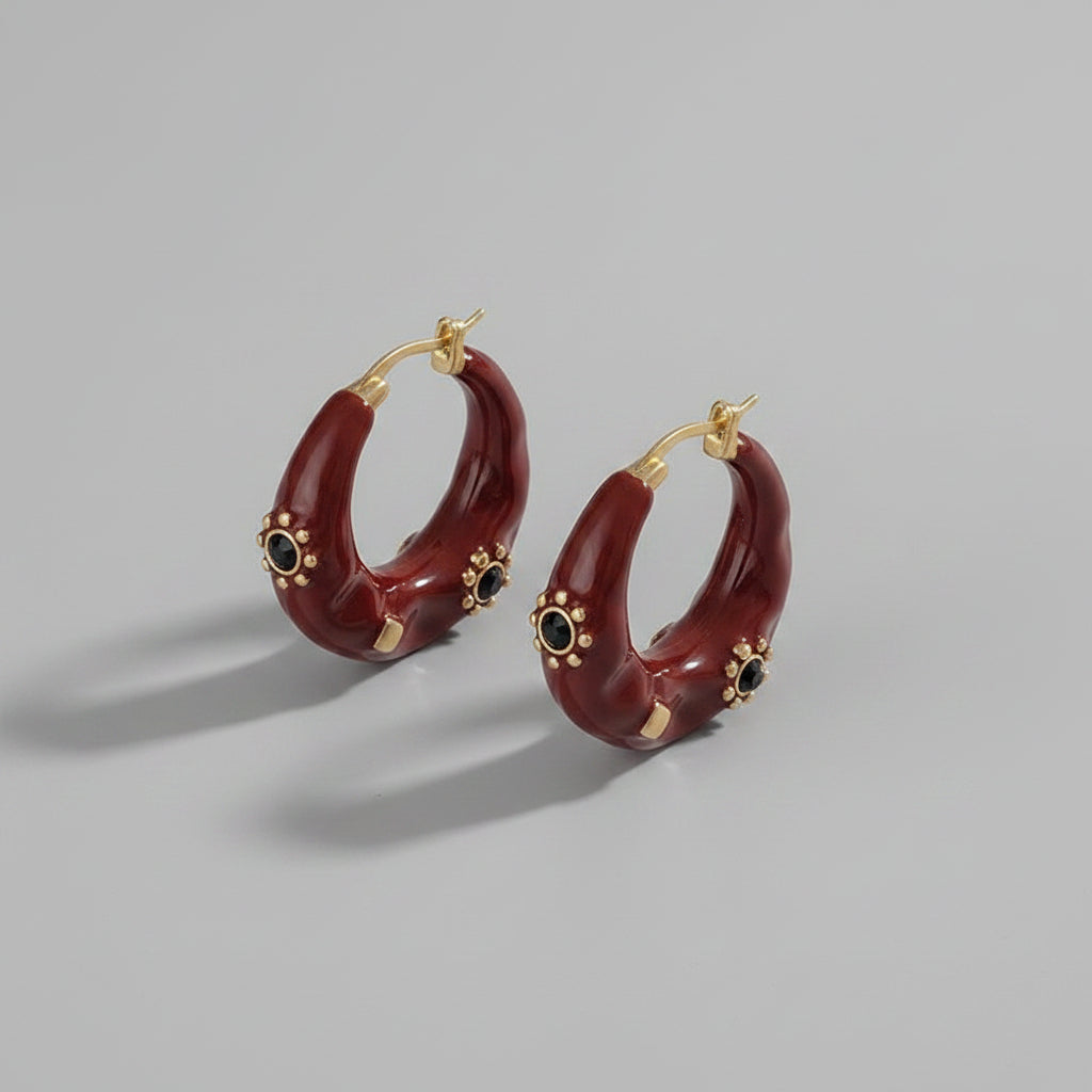 Red hoop earrings with gold accents on a piece of paper with text.