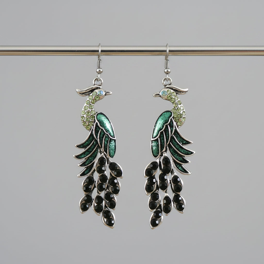 Pair of green and black leaf-shaped earrings hanging on a wooden rod with a blurred background.