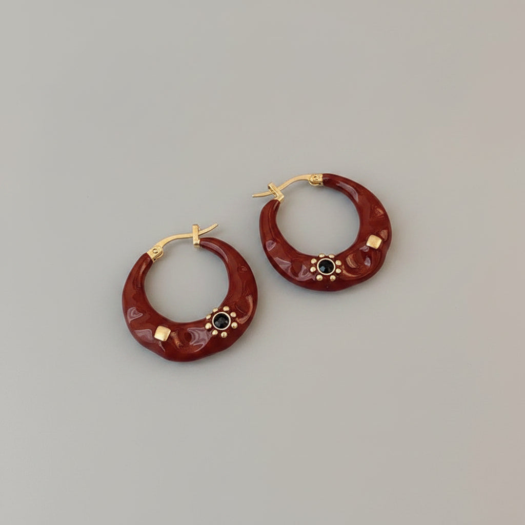 Red hoop earrings with gold accents on a black surface