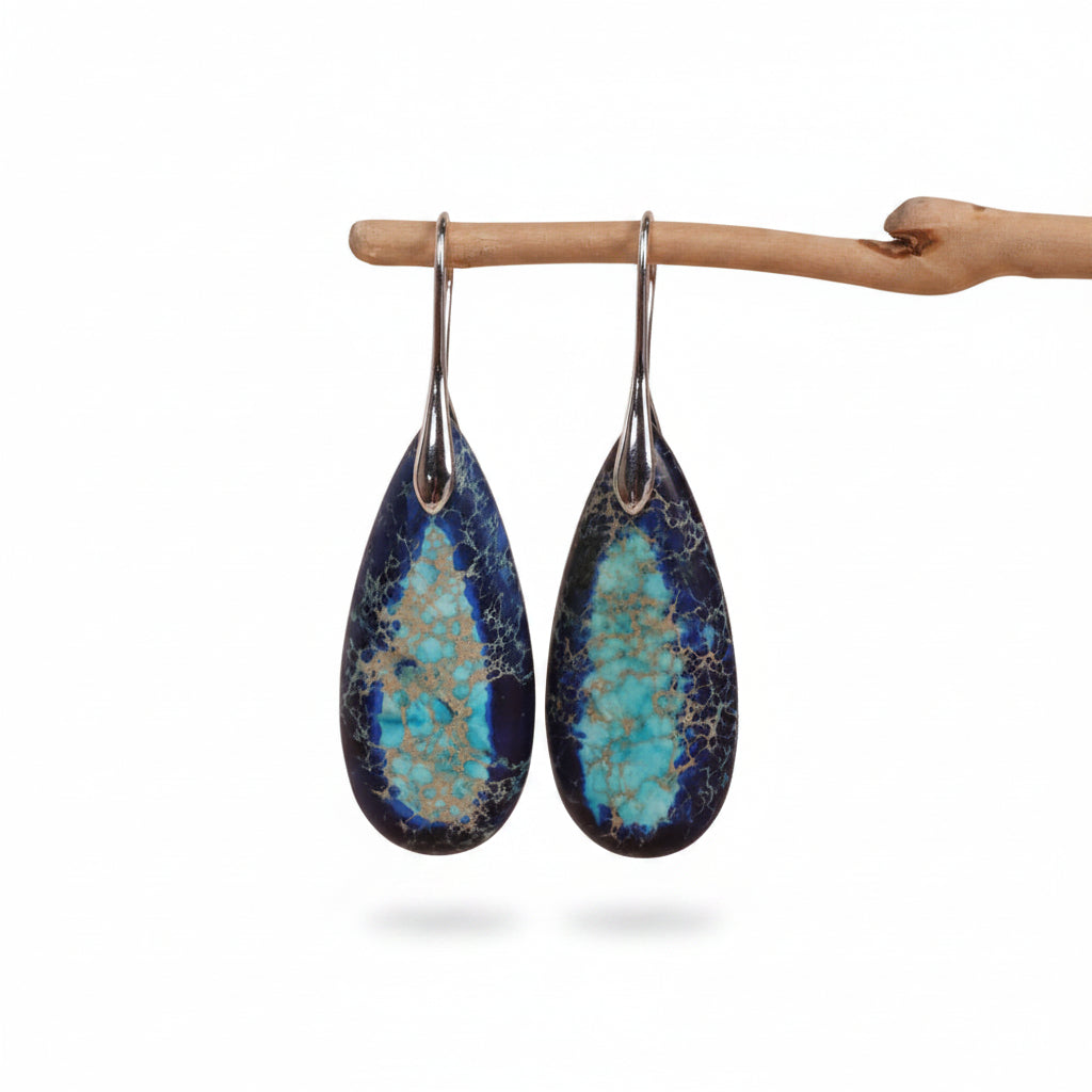 Teardrop-shaped earrings with blue and green marbled design hanging on a branch against a beige background