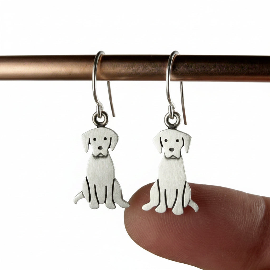 Dog-shaped earrings hanging from a rod with a hand holding one of them.