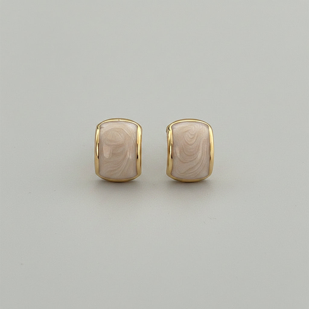 Gold and beige earrings held between fingers against a neutral background