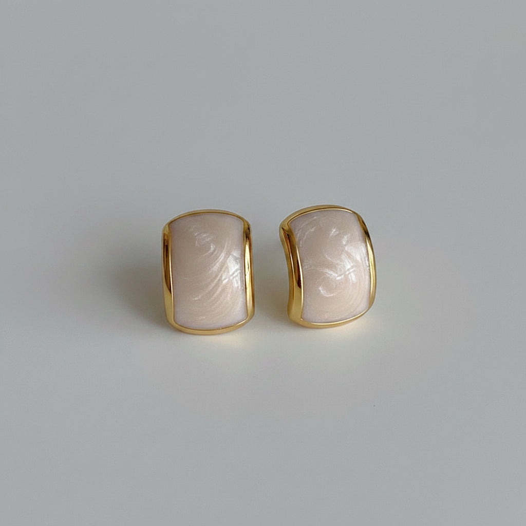 Gold-framed earrings with a textured stone-like center on a light gray background