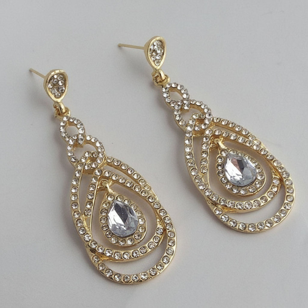 Gold and crystal teardrop earrings on a light gray background
