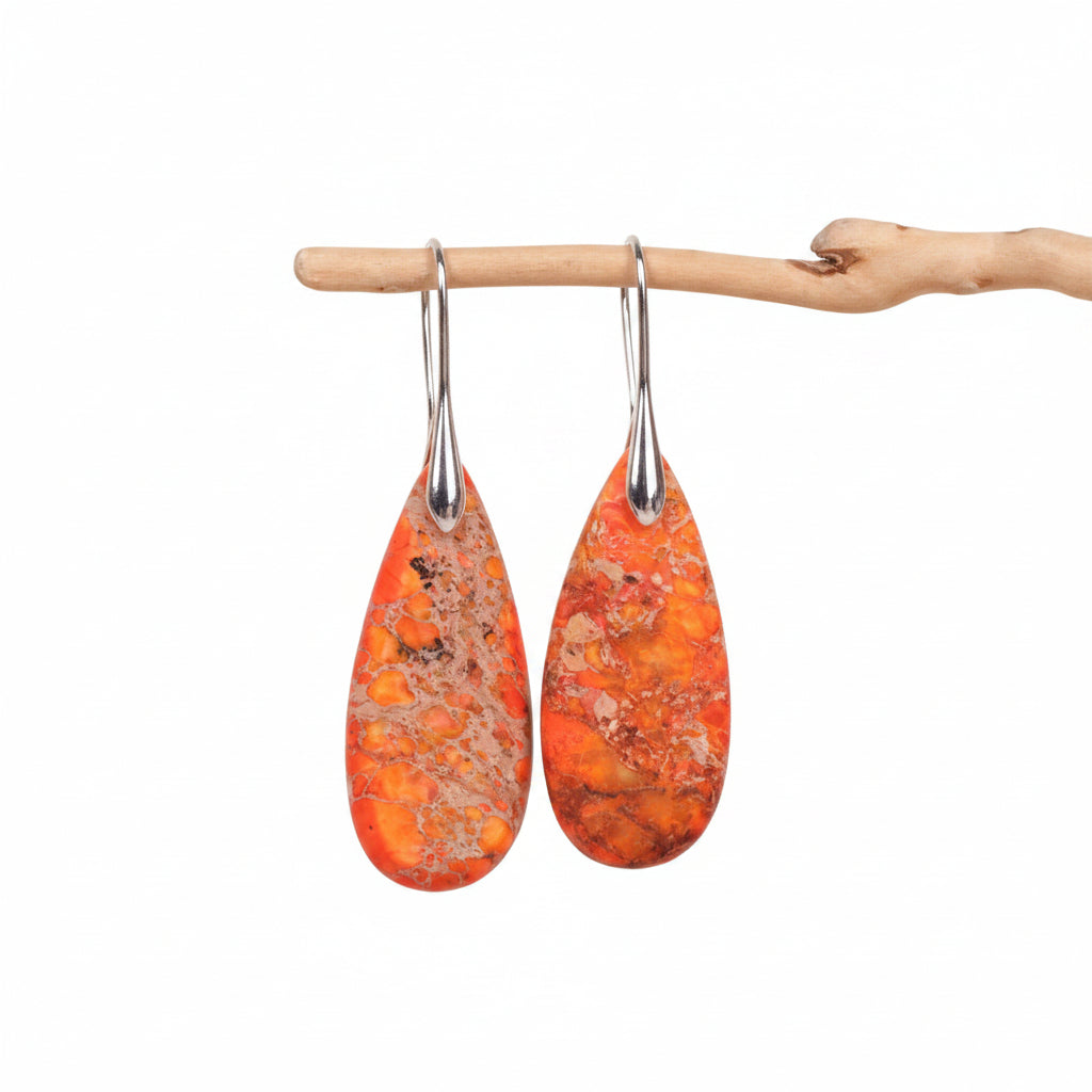 Teardrop-shaped orange earrings with silver hooks on a beige background