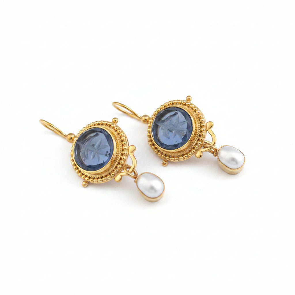 Pair of gold earrings with blue gemstones and white pearls on a gray background