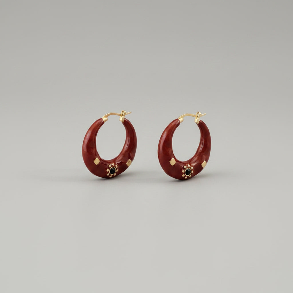 Red hoop earrings with gold accents on a textured surface