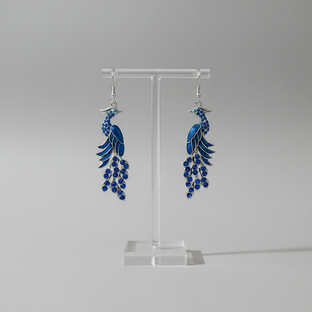 Blue peacock-shaped earrings hanging on a branch with a blurred natural background