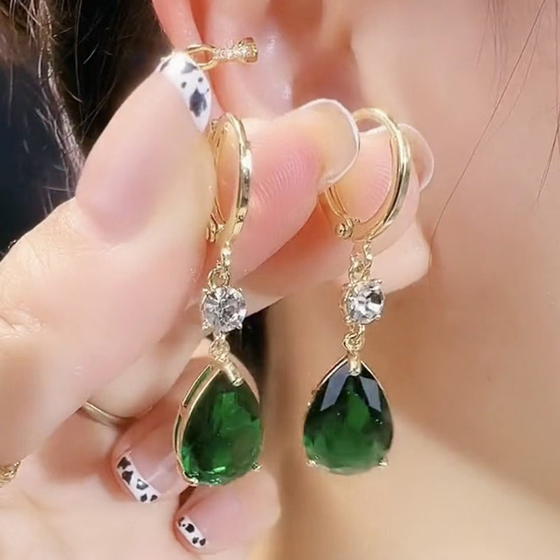 Gold earrings with green gemstones worn by a person