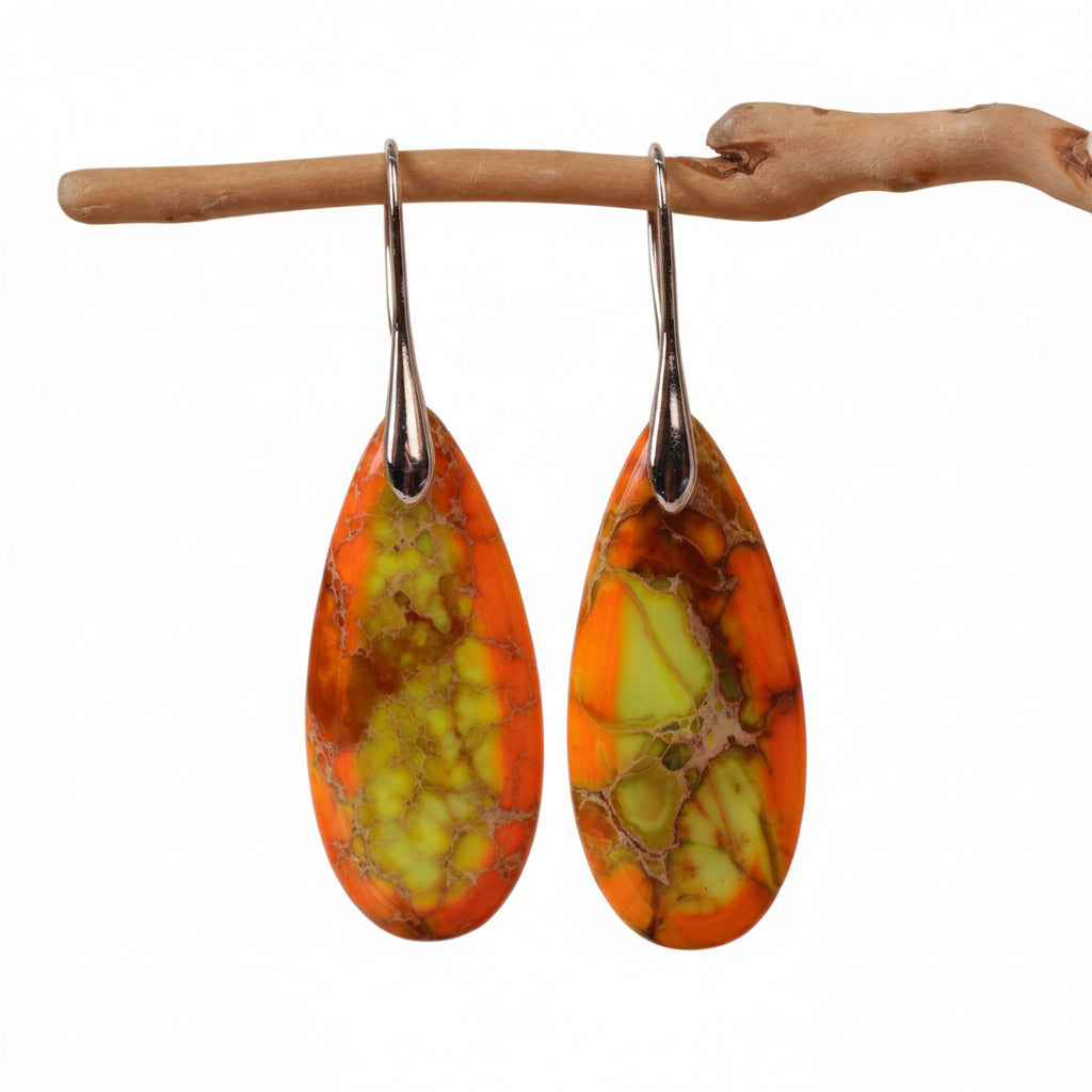 Pair of orange and green teardrop earrings hanging from a branch against a beige background