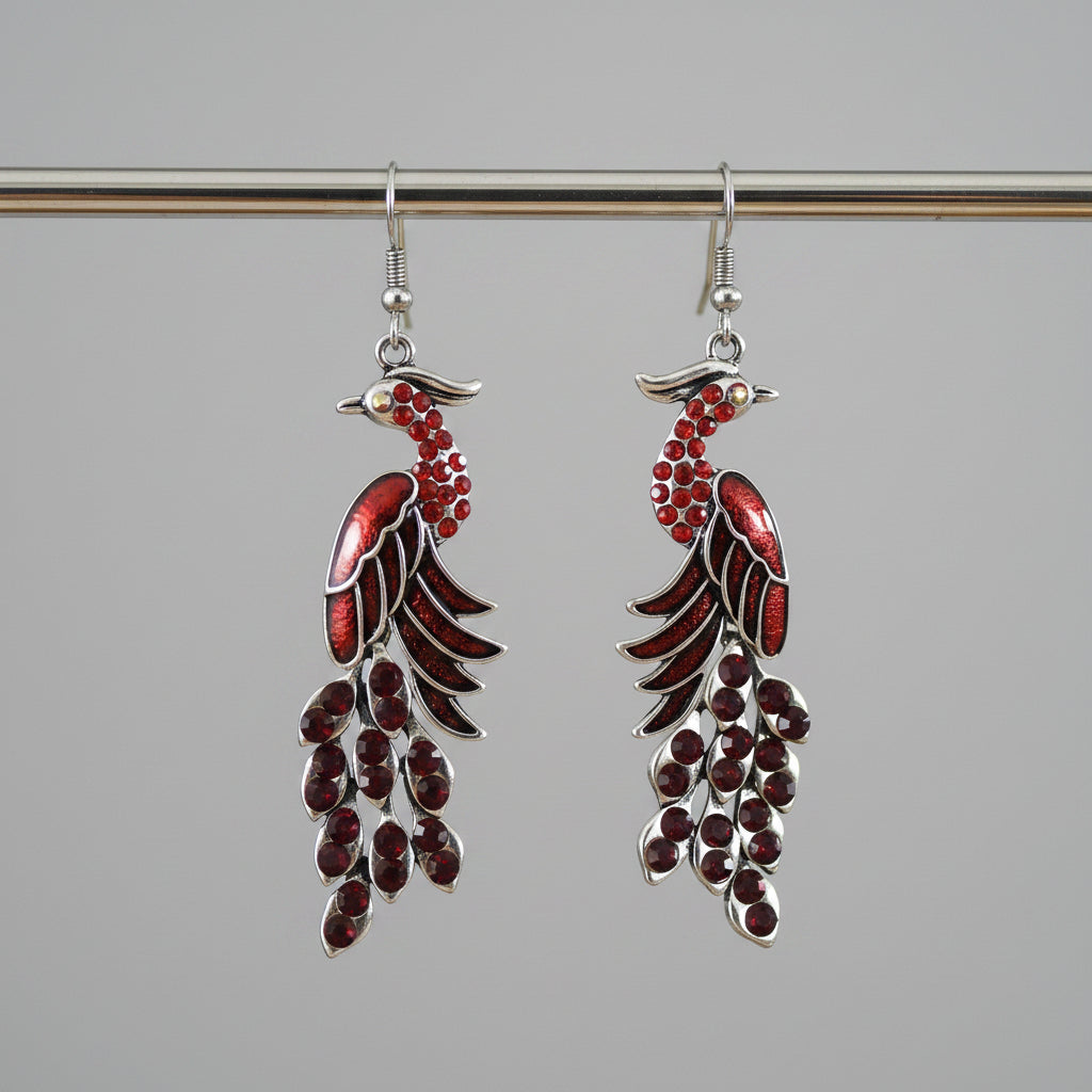 Red and silver feather-shaped earrings on a wooden stick with a blurred background