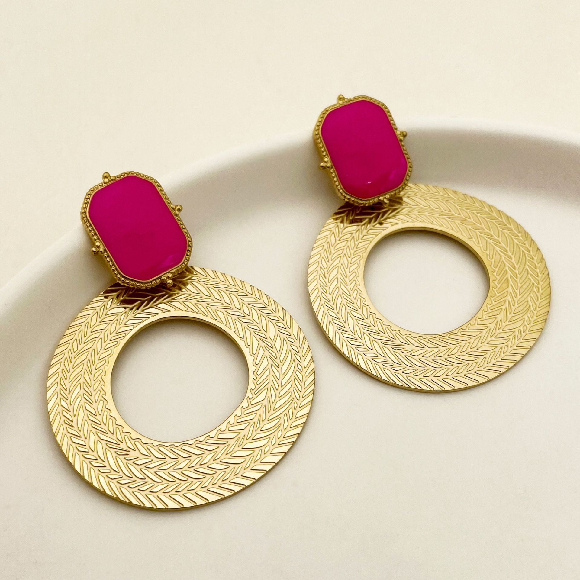 Gold earrings with pink gemstones on a beige background