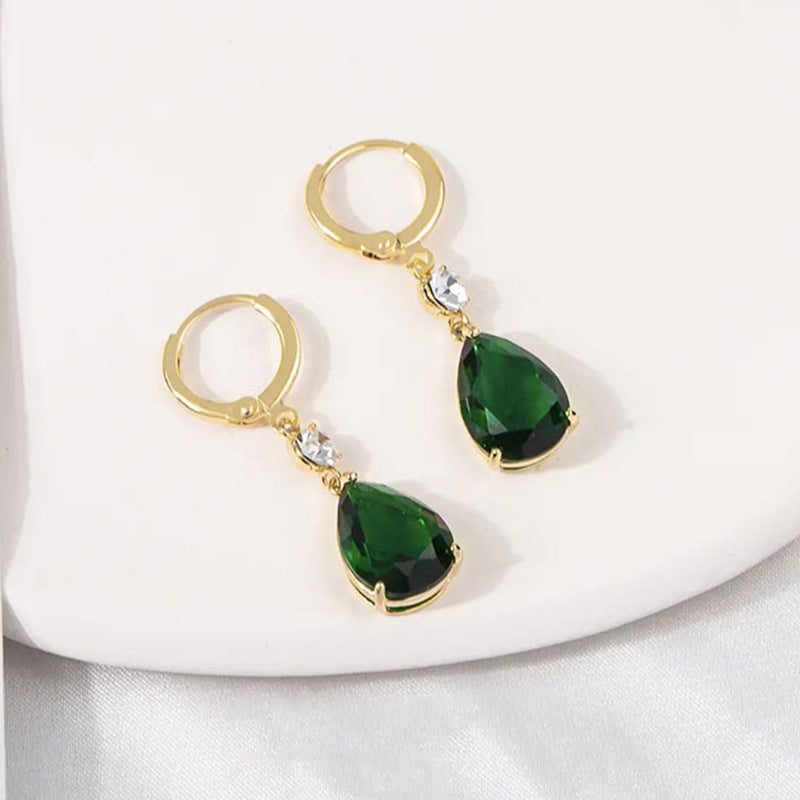Gold earrings with green teardrop stones on a white background