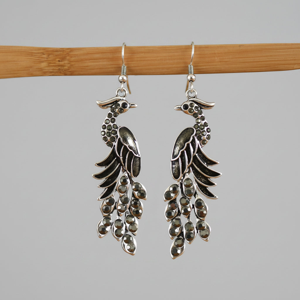 Silver peacock feather earrings on a wooden stick with a blurred background