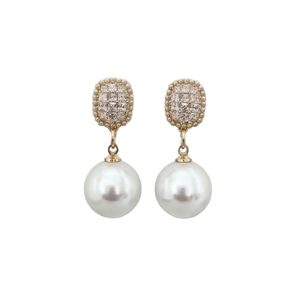 Pearl earrings with diamond-like top elements held by a hand against a neutral background