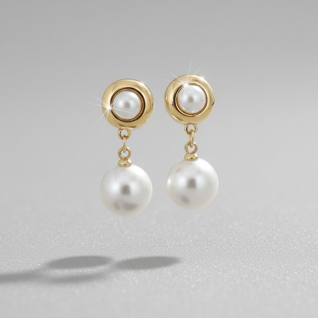 Pearl earrings with gold accents held by a hand against a neutral background