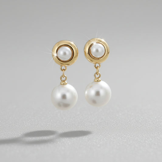 Pearl earrings with gold accents held by a hand against a neutral background