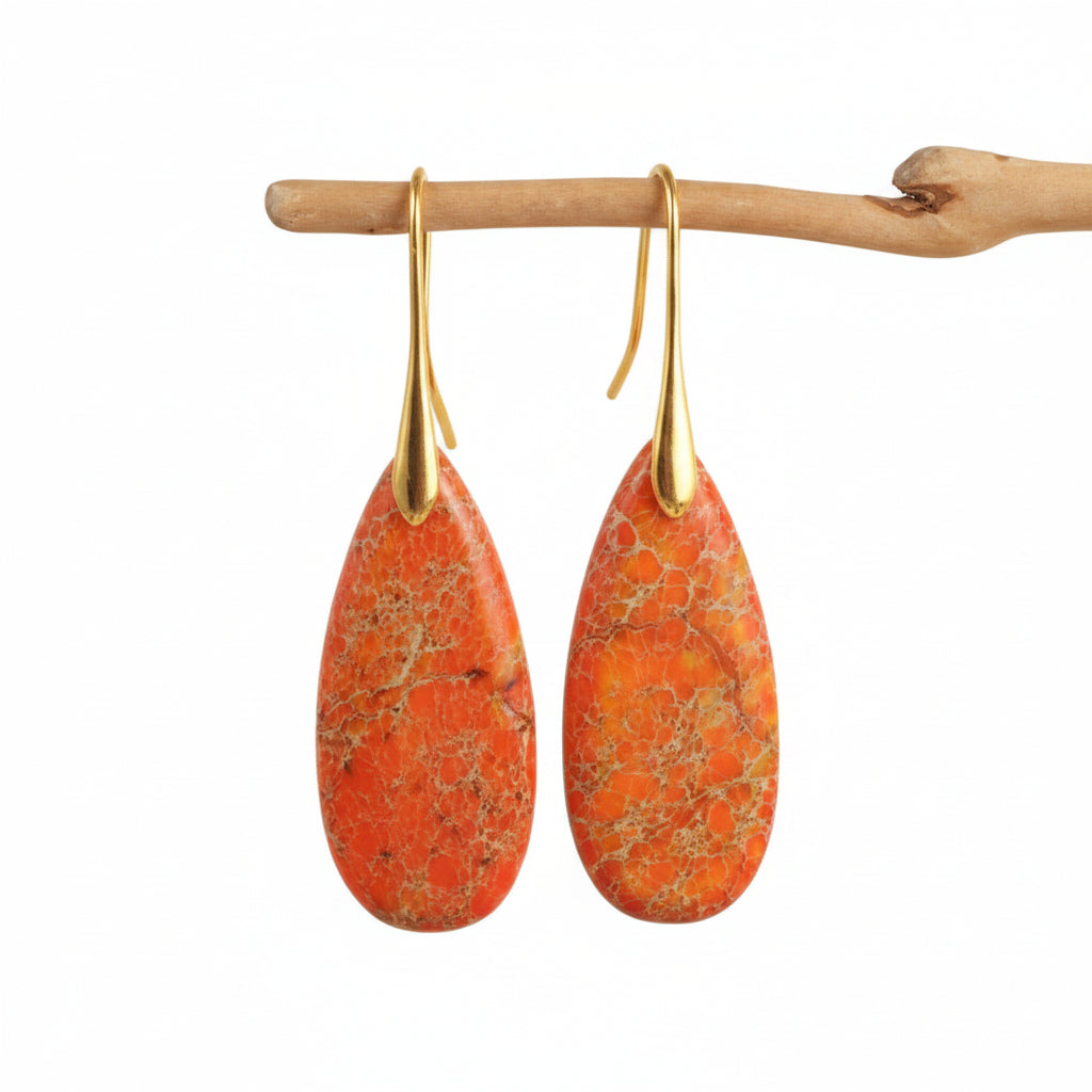 Teardrop-shaped orange earrings with gold hooks on a beige background