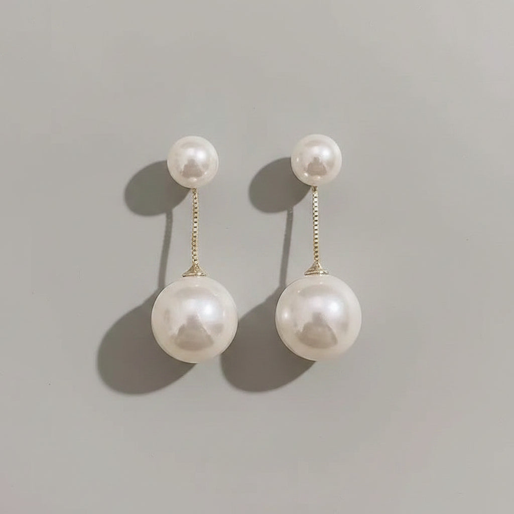 Pearl earrings held by a hand against a neutral background