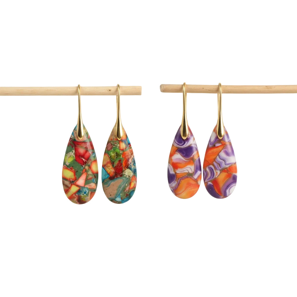 Colorful teardrop earrings with gold hooks on a wooden stick against a beige background