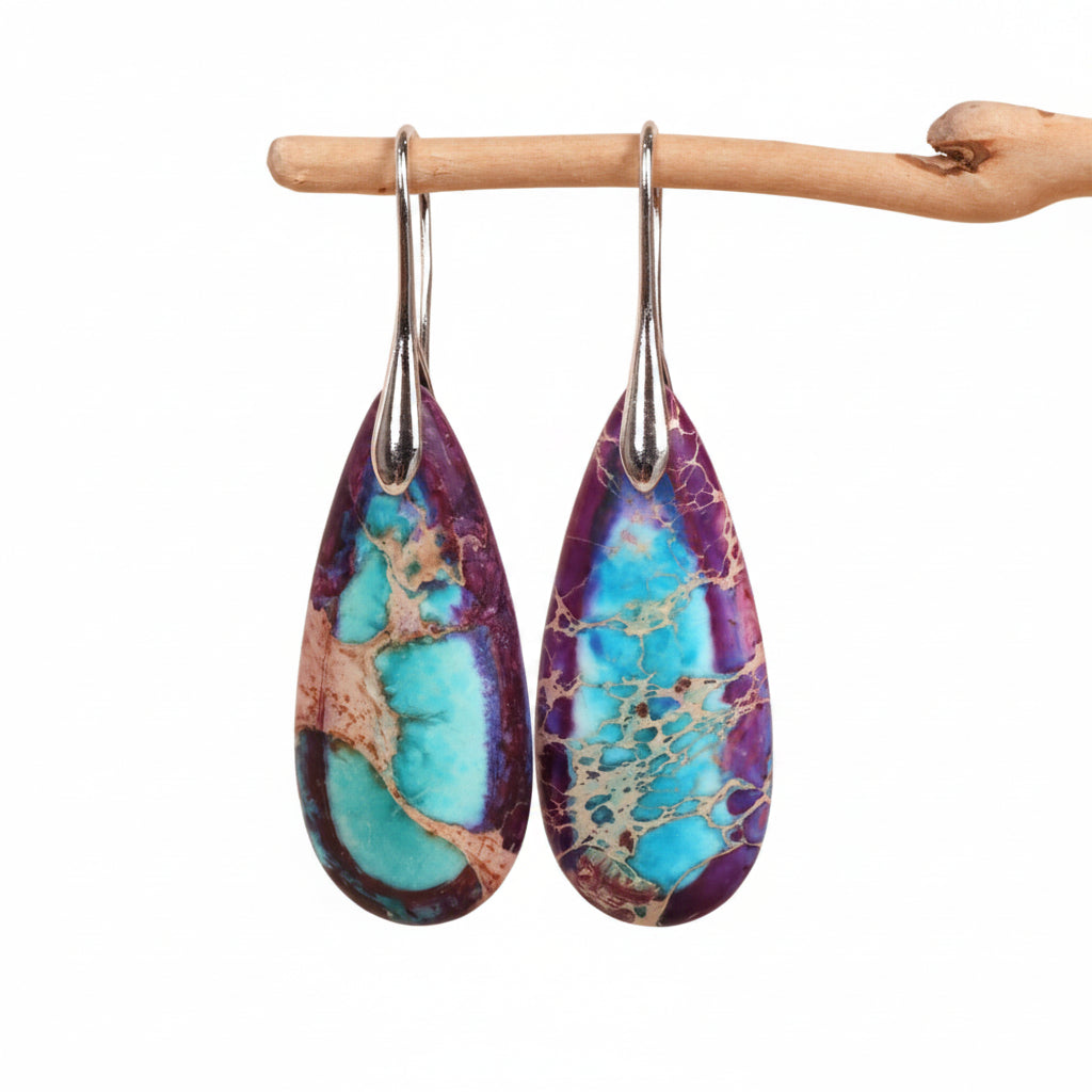 Teardrop-shaped earrings with purple and blue marbled design hanging on a wooden stick against a beige background.